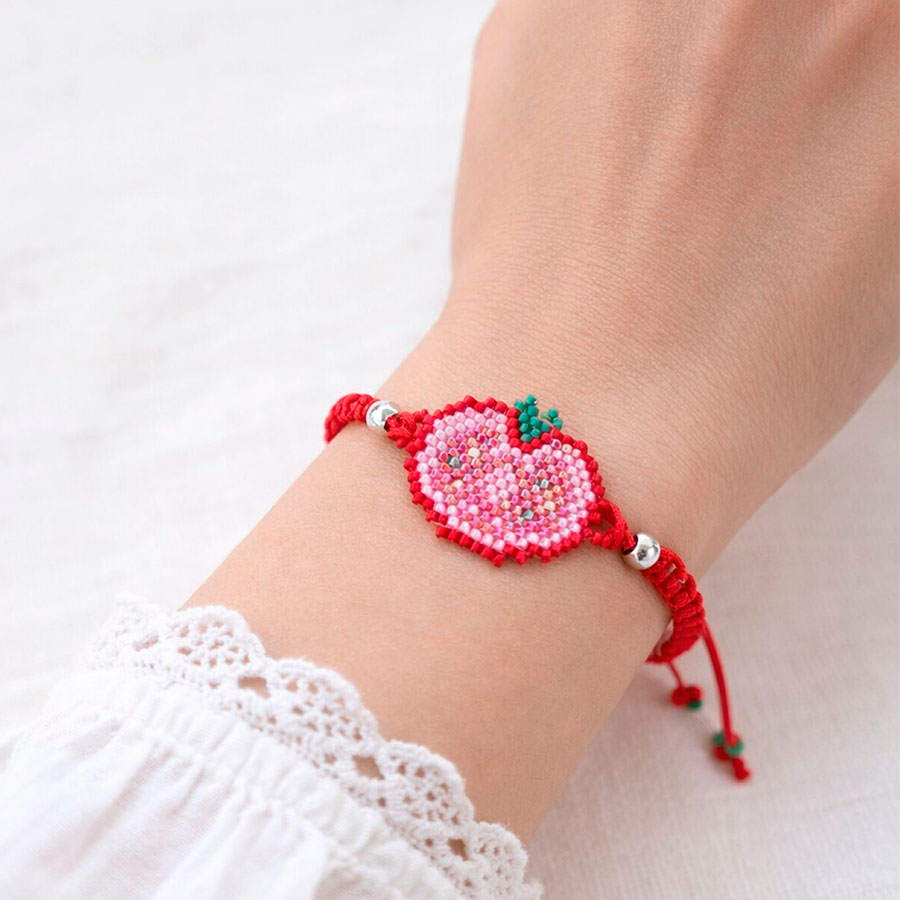 Pulsera Ajustable Tomate • Joyas Coquetas Pulsera ajustable tomate colocada en la muñeca, vista sobre una mano. Hecha a mano por Joyas Coquetas en España.