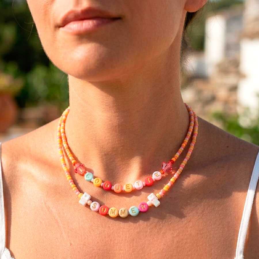 Collar nombres personalizado con primer plano de mujer con vestido blanco luciendo el pack de collar nombres "Summer" y "Coquette". Joyas hechas a mano en Málaga por Joyas Coquetas con cuentas de colores y estilo ibicenco.