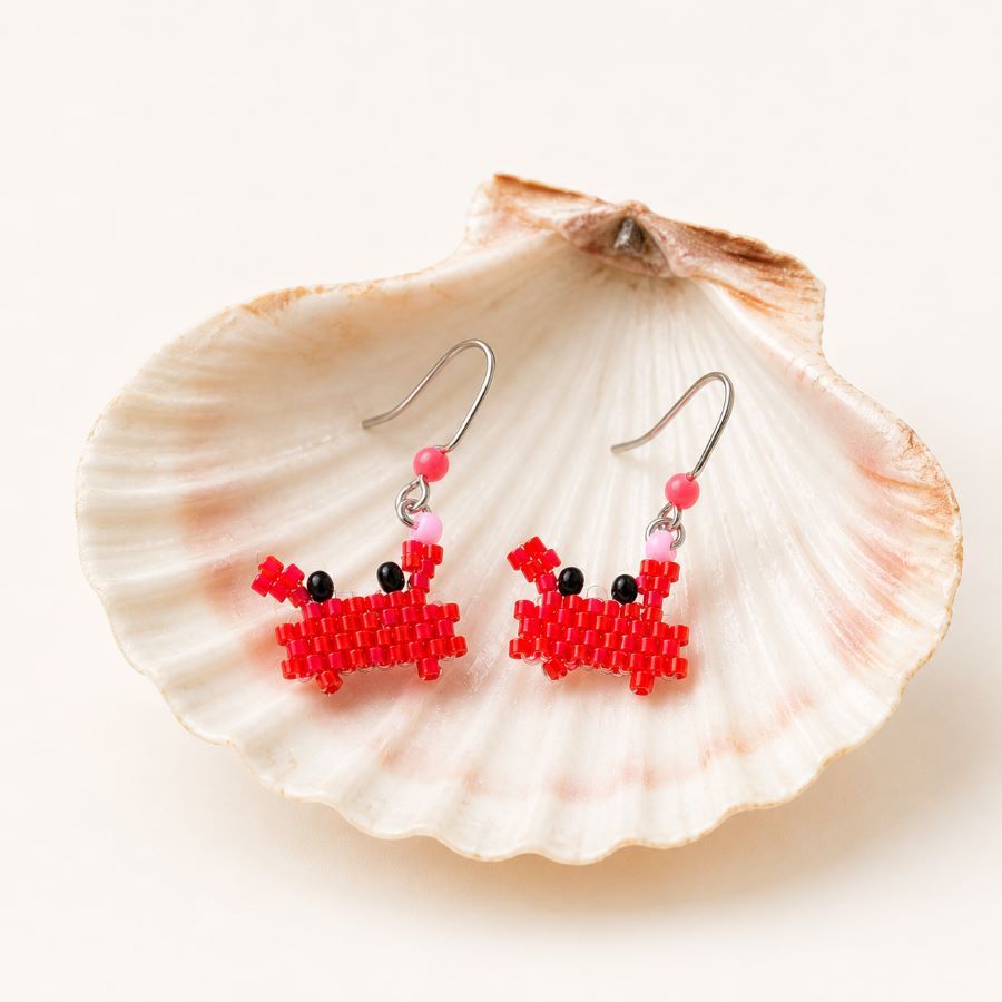 pendientes cangrejos rojos tejidos con cuentas Miyuki sobre un fondo neutro elegante con concha marina. Hecho en Málaga por Joyas Coquetas