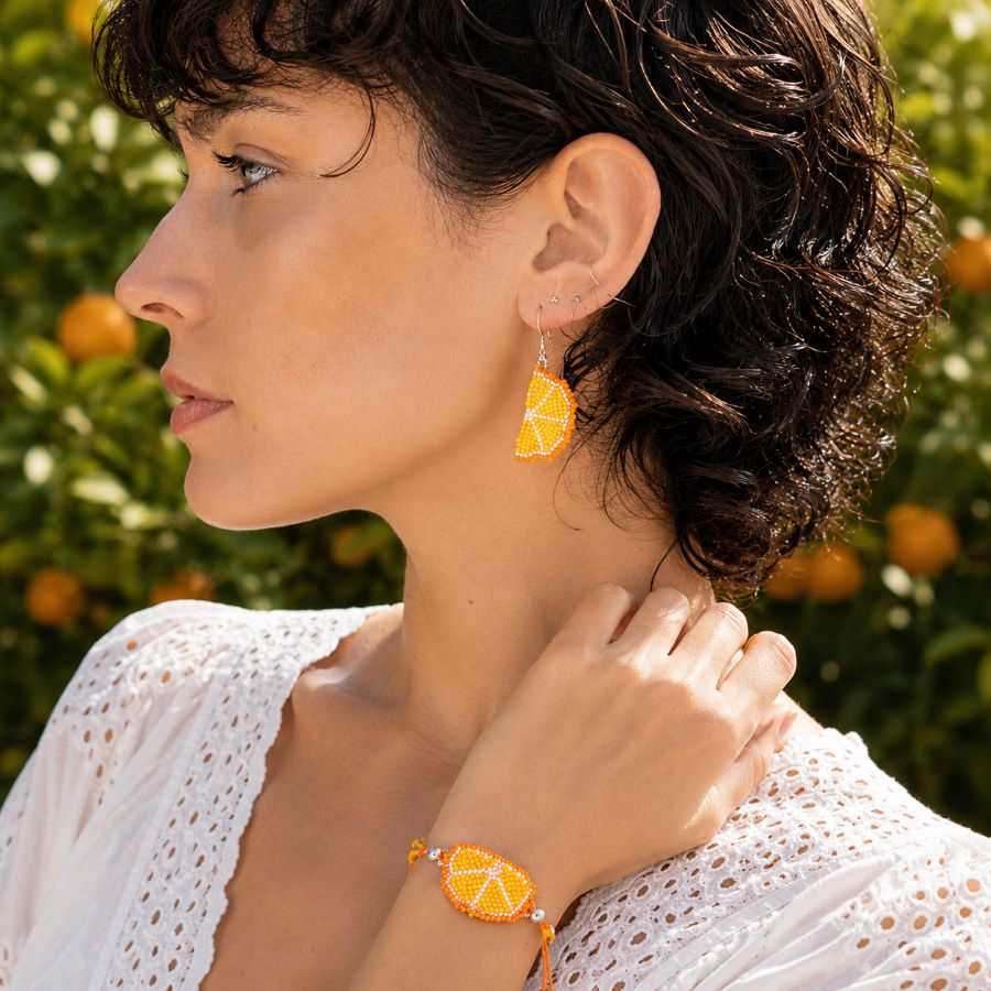 Pulsera Fruta Naranja Miyuki • Joyas Coquetas Modelo luciendo pulsera y pendientes de naranja Miyuki hechos a mano por Joyas Coquetas en Málaga, conjunto de joyería artesanal inspirada en una rodaja de naranja.