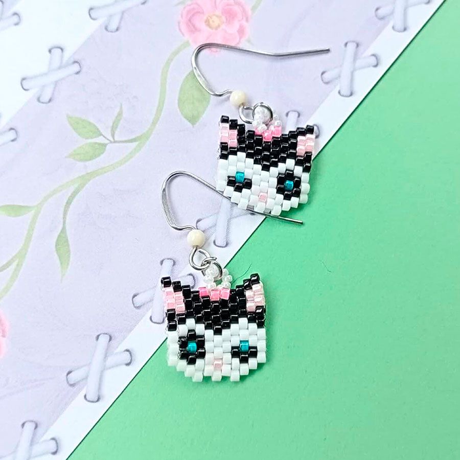 Joyas Coquetas y Divertidas hechas a mano • Joyas Coquetas Pendientes gata artesanales elaborados con la técnica del punto de ladrillo, presentados sobre un femenino diseño floral y una superficie verde menta. Hechos a mano por Joyas coquetas en España.