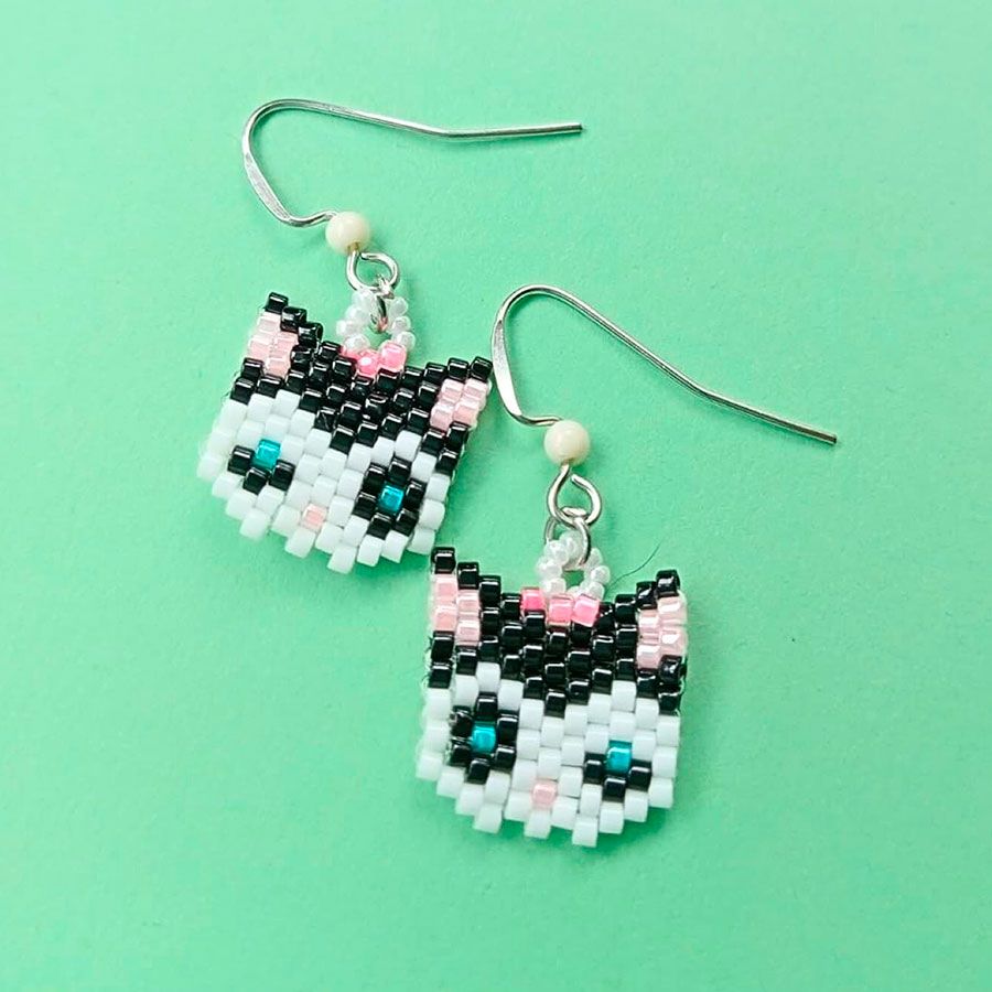 Pendientes Gata Artesanales • Joyas Coquetas Par de pendientes colgantes de gato hechos a mano con cuentas Miyuki negras, blancas y rosas sobre un fondo verde menta brillante. Hechos a mano por Joyas Coquetas en España.