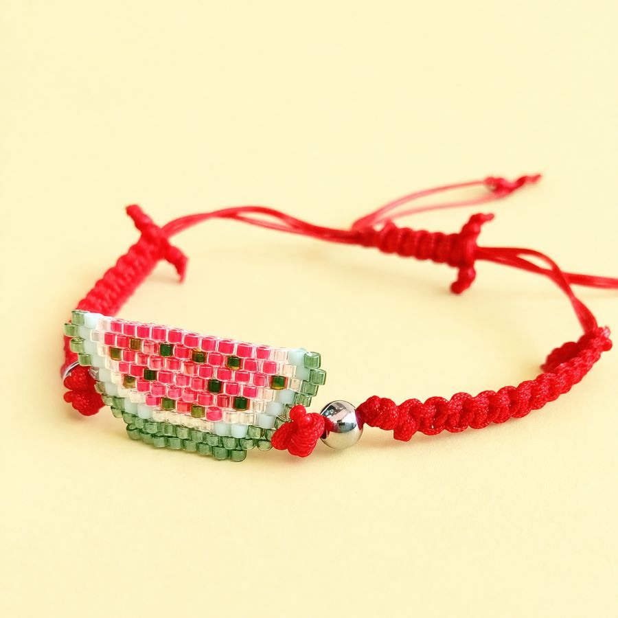 Pulsera sandía ajustable • Joyas Coquetas Pulsera sandía de cuentas Miyuki con cordón rojo ajustable sobre fondo color mantequilla. Hecha a mano por Joyas Coquetas en Málaga.