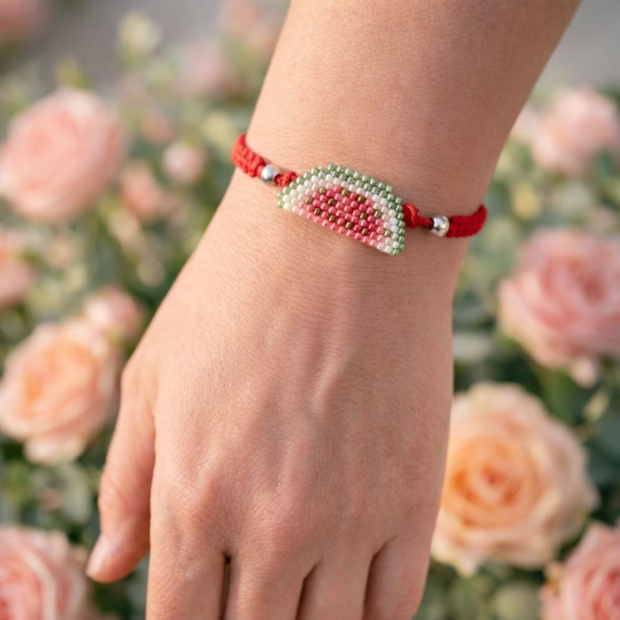 Pulsera sandía ajustable • Joyas Coquetas Imagen lifestyle de la pulsera ajustable sandía, sobre mano de mujer con fondo de flores. Hecha a mano en Málaga por Joyas Coquetas